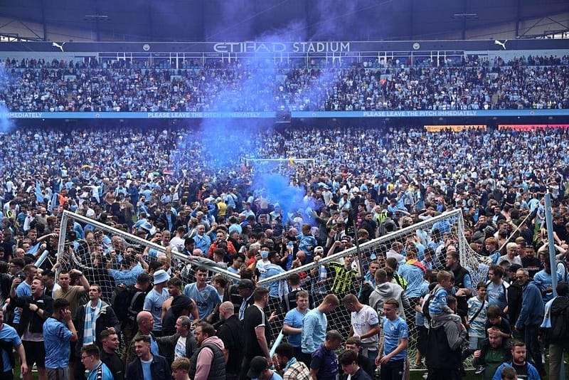 Fans invading a football pitch during a match, highlighting the excitement and controversy of pitch invasions in modern football.